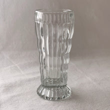 Load image into Gallery viewer, Vintage clear wavy ribbed 5oz footed juice glass tumbler. Crafted by Jeannette Glass, USA, 1920s. The sweetest little tumbler is known to be hard to find in this size and has lovely details. It could be easily repurposed as a bud vase for a wee floral bouquet, or to store make-up brushes.
In excellent used condition, no chips.
Measures 2 x 4 1/2 inches
Capacity 5 ounces