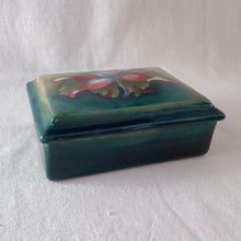 Load image into Gallery viewer, A lovely vintage "Columbine" dresser box with a jewel-toned flower against a green wash ground. Design by Walter Moorcroft and produced by Moorcroft Pottery, England, circa 1950. Stamped with the WM Moorcroft signature and "Made in England" along with paper label having the Royal Warrant and "By Appointment, Potter to the late Queen Mary". In excellent condition, free from chips, cracks, repairs; crazing present. Measures 4.75" x 3.5" x 2"
