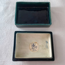 Load image into Gallery viewer, A lovely vintage "Columbine" dresser box with a jewel-toned flower against a green wash ground. Design by Walter Moorcroft and produced by Moorcroft Pottery, England, circa 1950. Stamped with the WM Moorcroft signature and "Made in England" along with paper label having the Royal Warrant and "By Appointment, Potter to the late Queen Mary". In excellent condition, free from chips, cracks, repairs; crazing present. Measures 4.75" x 3.5" x 2"