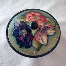 Load image into Gallery viewer, Vintage mid-century "Clematis" lidded dish with green ground lid and teal/blue ground on bowl's interior and deep blue on the exterior of the bowl. The colours are vibrant and the tube lining and hand painting are spectacular. Produced by Moorcroft Pottery, England, circa 1950s.  Measures 6-1/4" x 3-1/2"  Excellent condition. No cracks or chips. Normal crazing for a piece of this age. Impressed marks include Walter Moorcroft's signature, Potter to H.M. The Queen and Made in England.