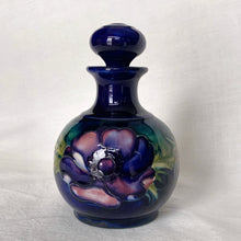 Load image into Gallery viewer, Vintage mid-century "Anemone" perfume bottle with stopper. Hand painted in the slip glaze technique in shades of purple, pink and green on a deep cobalt blue ground. Produced by Moorcroft Pottery, circa 1928-1953. In excellent condition, no chips, cracks or repairs, crazing present. Bottom shows impressed signature of Walter Moorcroft, "MADE IN ENGLAND" and Royal Warrant paper label - 'Potter To HM The Queen'. Measures 4" x 5-1/2"