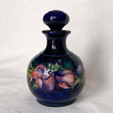 Load image into Gallery viewer, Vintage mid-century "Anemone" perfume bottle with stopper. Hand painted in the slip glaze technique in shades of purple, pink and green on a deep cobalt blue ground. Produced by Moorcroft Pottery, circa 1928-1953. In excellent condition, no chips, cracks or repairs, crazing present. Bottom shows impressed signature of Walter Moorcroft, "MADE IN ENGLAND" and Royal Warrant paper label - 'Potter To HM The Queen'. Measures 4" x 5-1/2"