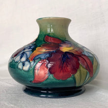 Load image into Gallery viewer, Gorgeous vintage mid-century hand painted squat flower vase in the "Orchid" pattern on green ground, hand painted in shades of red, yellow, purple and blue using the slip glaze technique. Made by Moorcroft Pottery in Stoke-on-Trent, England, circa 1950. In excellent condition, no chips, cracks or repairs, crazing present. Initials of Walter Moorcroft in blue, impressed marks "MOORCROFT" and "MADE IN ENGLAND". Measures 3-1/4" high