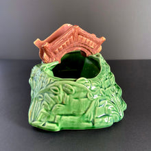 Load image into Gallery viewer, A vintage ceramic planter featuring a rusty red bridge over a green pond with impressed brick wall and stairs, and floral details. Crafted by Shawnee Pottery, USA, 1950s. Create a unique garden with this unique planter!
In vintage condition with minor flea bites to the bridge.
Measures 9 x 5 3/4 x 4 3/4 inches