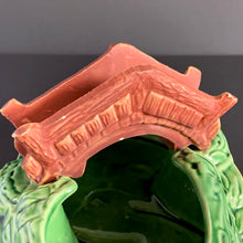 Load image into Gallery viewer, A vintage ceramic planter featuring a rusty red bridge over a green pond with impressed brick wall and stairs, and floral details. Crafted by Shawnee Pottery, USA, 1950s. Create a unique garden with this unique planter!
In vintage condition with minor flea bites to the bridge.
Measures 9 x 5 3/4 x 4 3/4 inches