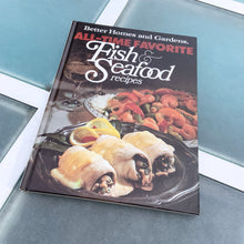 Load image into Gallery viewer, Better Homes and Gardens is known for its fabulous cookbooks. This hardcover cookbook focuses on their all-time favourite fish and seafood inspired recipes. Its 96 pages are filled with amazing recipes along with many colour photographs. Originally published by Meredith Corporation, USA, 1980. This is the large format edition, first printing 1983.   In great vintage condition with normal age-related yellowing.
