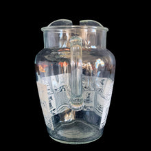 Load image into Gallery viewer, Vintage 64 oz clear glass ice lip pitcher with ribbed handle features a block printed design early American heritage scenes in white with a band of gold eagles and stars. Crafted by Anchor Hocking, USA, 1950s. A great way to show off your patriotic style!

In excellent condition, no chips, minor wear to the gold.

Measures 6 1/2 x 5 1/2 x 9 inches

Capacity 64 ounces
