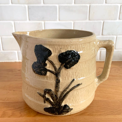 Vintage natural yellow ware strapped barrel milk pitcher featuring black lily in bas relief with rope style handle, No. 21171. Crafted by Robinson Ransbottom Pottery Co., USA, 1930s. A beautiful piece of primitive farmhouse tableware to enhance your home's decor and a wonderful addition to any art pottery collection!

Measures 5 1/4 x 5 1/4 inches. In as found vintage condition, chip to rim, no cracks/repairs, glaze wear at the spout, age-related crazing and glaze pops. Unmarked. Capacity 48 ounces