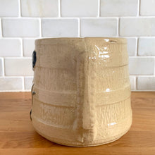 Load image into Gallery viewer, Vintage natural yellow ware strapped barrel milk pitcher featuring black lily in bas relief with rope style handle, No. 21171. Crafted by Robinson Ransbottom Pottery Co., USA, 1930s. A beautiful piece of primitive farmhouse tableware to enhance your home&#39;s decor and a wonderful addition to any art pottery collection!

Measures 5 1/4 x 5 1/4 inches. In as found vintage condition, chip to rim, no cracks/repairs, glaze wear at the spout, age-related crazing and glaze pops. Unmarked. Capacity 48 ounces

