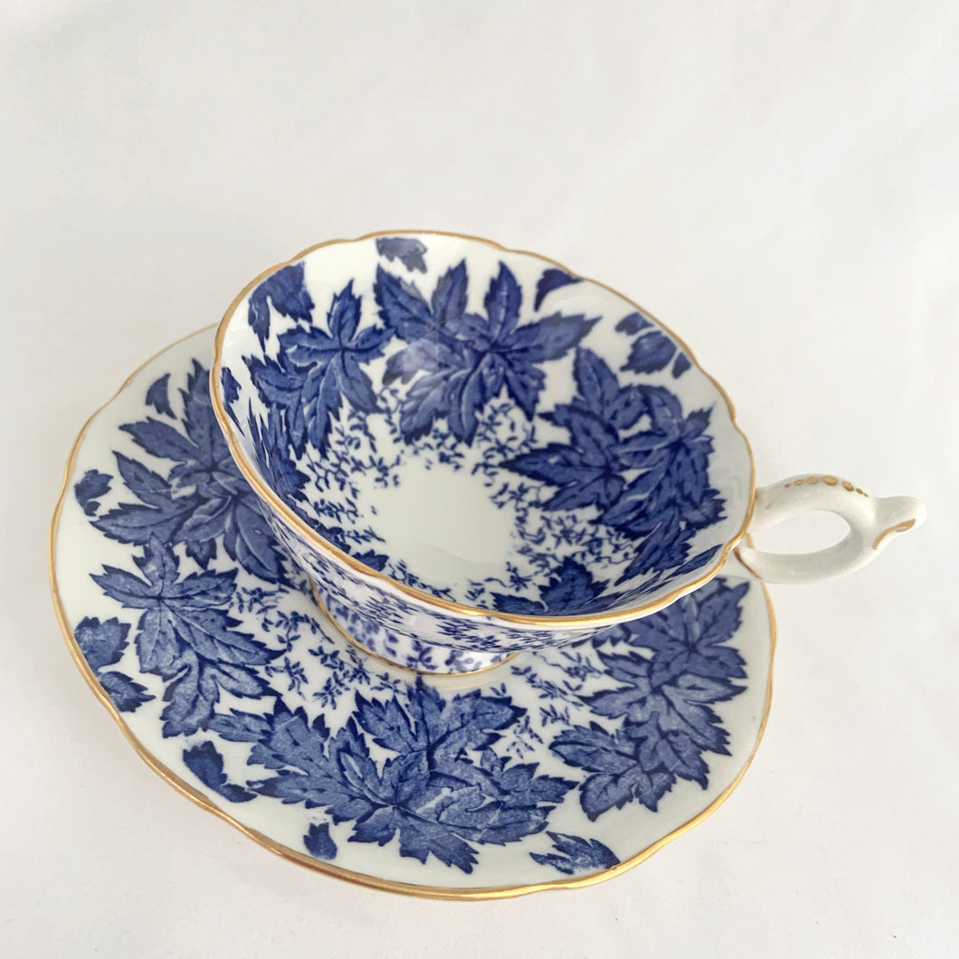 Antique bone china teacup and saucer with a subtle scalloped edge with transferware pattern of cobalt blue maple leaves, French loop handle with thumb rest, and edges trimmed with gold gilt. Crafted by Coalport, England, circa 1920s. In excellent condition, free from chips, cracks and repairs. Marked 