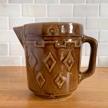 Load image into Gallery viewer, Vintage glossy caramel brown stoneware pitcher featuring a castle turret with diamonds detail. Crafted by Monmouth Western Stoneware, USA, 1920s. Add this utilitarian piece to your farmhouse decor or art pottery collection!

In excellent condition, no chips/cracks/repairs, age-related crazing. Unmarked.

Measures 4 1/2 x 5 inches
