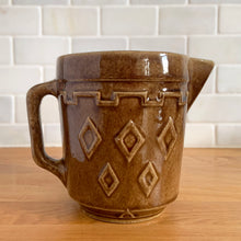 Load image into Gallery viewer, Vintage glossy caramel brown stoneware pitcher featuring a castle turret with diamonds detail. Crafted by Monmouth Western Stoneware, USA, 1920s. Add this utilitarian piece to your farmhouse decor or art pottery collection!

In excellent condition, no chips/cracks/repairs, age-related crazing. Unmarked.

Measures 4 1/2 x 5 inches
