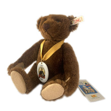 Load image into Gallery viewer, Vintage 150th Anniversary bear is made brown mohair. Brown hand embroidered nose and claws, brown glass eyes with black pupils, and light beige felt hand and foot pads. Flat foot pads enable it stand. Has a squeaker and is fully jointed. Gold satin ribbon with porcelain medallion displays a picture of Margarete Steiff. Brass button-in-ear red and white tag, and two paper tags. A must-have for any Steiff or teddy bear collector! In excellent condition. Measures 11 inches or 28cm tall
