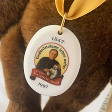 Load image into Gallery viewer, Vintage 150th Anniversary bear is made brown mohair. Brown hand embroidered nose and claws, brown glass eyes with black pupils, and light beige felt hand and foot pads. Flat foot pads enable it stand. Has a squeaker and is fully jointed. Gold satin ribbon with porcelain medallion displays a picture of Margarete Steiff. Brass button-in-ear red and white tag, and two paper tags. A must-have for any Steiff or teddy bear collector! In excellent condition. Measures 11 inches or 28cm tall
