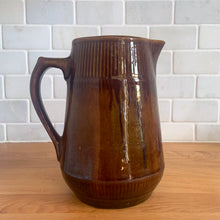 Load image into Gallery viewer, Vintage gloss brown stoneware pitcher with ribbed bands. Crafted by Medalta Stoneware, Canada, 1924. This utilitarian piece nicely complement any farmhouse or cottage kitchen!

In as found vintage condition, no chips/repairs, 3 hairline cracks, age-related wear to the exterior. Unmarked.

Measures 6 3/8 x 7 1/4 inches
