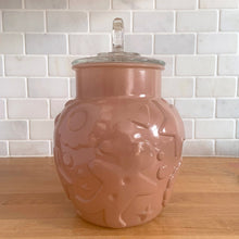 Load image into Gallery viewer, Vintage mid-century chocolate brown glass cookie jar with embossed gingerbread men, donuts, stars and cookies with clear ring handled lid. Crafted by Hazel-Atlas Glass, USA, 1950s. Use this nice sized jar to store cookies or dry goods and add whimsy to your kitchen decor.

In vintage condition with chips to the interior rim of the jar. The lid is in excellent condition, no chips.

Measures 6 1/2 x 10 inches
