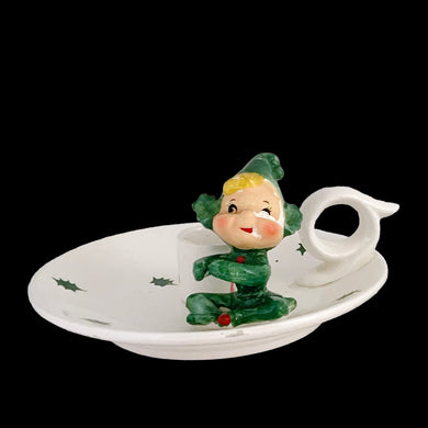 Vintage mid-century white ceramic candle holder with seated green pixie elf, holly leaves and finger ring. Crafted by Holt Howard, Japan, 1959. This highly collectible kitschy candle holder is the perfect accent for your Christmas holiday display!

In as found condition, roughness on rim of the plate and paint loss on pixie's face.

Measures 5 1/2 x 2 1/2