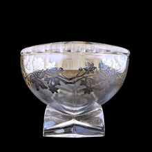 Load image into Gallery viewer, This exquisite vintage flowerlite features a clear oval or oblong shape adorned with a delicate silver overlay of orchid flowers. Crafted by Viking Art Glass in the 1950s, it includes a glass flower frog designed to hold two taper candles and rests on elegant Chinoiserie-style scrolled feet. Ideal for creating sophisticated floral arrangements, this Hollywood Regency piece enhances any space with timeless charm, whether illuminated by candlelight or displayed on its own in both modern and vintage interiors.
