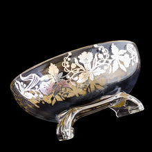 Load image into Gallery viewer, This exquisite vintage flowerlite features a clear oval or oblong shape adorned with a delicate silver overlay of orchid flowers. Crafted by Viking Art Glass in the 1950s, it includes a glass flower frog designed to hold two taper candles and rests on elegant Chinoiserie-style scrolled feet. Ideal for creating sophisticated floral arrangements, this Hollywood Regency piece enhances any space with timeless charm, whether illuminated by candlelight or displayed on its own in both modern and vintage interiors.
