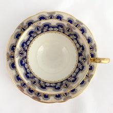 Load image into Gallery viewer, Antique bone china teacup and saucer is absolutely stunning! Both have a subtle scalloped shape. The white cup is decorated in a design of pale blue floral bouquets and bows on a cobalt blue band with gold gilt details. Produced by Aynsley, England. Excellent condition, free from chips, cracks and repairs. The pattern number 3410 is painted on the saucer. The stamped maker&#39;s mark indicates production between 1905 - 1925. Teacup measures 3 1/2 x 2 1/4 inches | Saucer measures 5 5/8 inches
