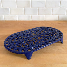 Load image into Gallery viewer, Vintage cobalt blue oval shaped cast iron trivet with floral design. Made in Taiwan, 1970s. Use as intended or as wall decor. A charming addition to any kitchen!

In excellent condition. Comes with a hanger on the back.

Measures 10 x 5 7/8 x 7/8 inches
