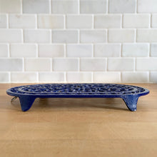 Load image into Gallery viewer, Vintage cobalt blue oval shaped cast iron trivet with floral design. Made in Taiwan, 1970s. Use as intended or as wall decor. A charming addition to any kitchen!

In excellent condition. Comes with a hanger on the back.

Measures 10 x 5 7/8 x 7/8 inches
