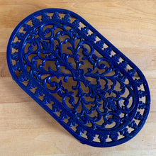 Load image into Gallery viewer, Vintage cobalt blue oval shaped cast iron trivet with floral design. Made in Taiwan, 1970s. Use as intended or as wall decor. A charming addition to any kitchen!

In excellent condition. Comes with a hanger on the back.

Measures 10 x 5 7/8 x 7/8 inches

