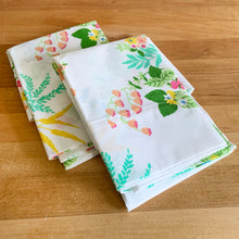 Load image into Gallery viewer, This is a gorgeous set of vintage white poly cotton blend standard size Ultracale pillowcases featuring a colourful pattern of flowers and berries. Crafted by Wamsutta Mills, USA, circa 1970s. This colourful  print brings so much fun and energy to your home decor or repurpose the fabric for crafts or clothing!  These pillowcases appear to be new old stock and are in excellent condition, the colours are vibrant and the fabric is crisp.   Measures 20 1/2 x 30 1/2 inches

