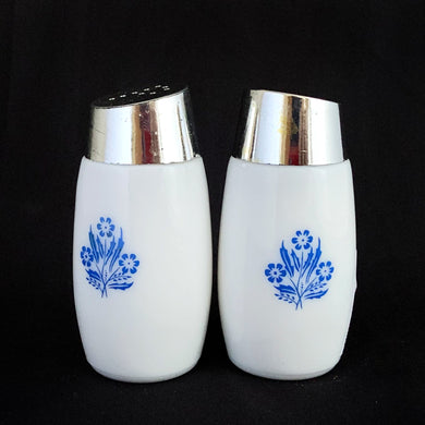 A classic set of vintage white milk glass salt and pepper shakers decorated with blue cornflowers with chrome lids with holes in the shape of an 