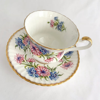 Stunning vintage white porcelain teacup and matching saucer featuring pink cornflowers and blue flowers plus gold gilt details with a spray of flowers on the interior of the teacup. Produced by The Paragon China Company, England, circa 1950s.  In excellent condition, free from chips/cracks/repairs. Marked on the bottom with single warrant stamp.  Teacup measures 3 1/8 x 2 3/4 inches  Saucer measures 5 3/8 inches