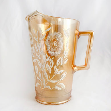 A lovely marigold carnival glass pitcher featuring the Cosmos floral pattern in white. Produced by the Jeannette Glass Company, USA, between 1950-1970. Perfect for serving your favourite beverage with vintage flare!   All pieces are in excellent condition, no chips or wear.  Measures 4 1/2 x 6 3/4 inches tall  Capacity 32 ounces   
