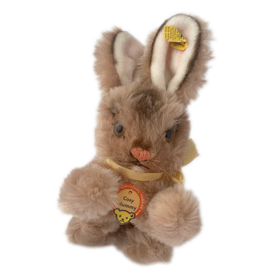 Vintage stuffed animal tan light brown bunny rabbit. Washable Dralon plush material. Hand embroidered pink nose and brown mouth, brown glass eyes with black pupils, and light beige felt rear foot pads. Gold satin ribbon and round red, blue and yellow tag bearing the name Cosy Mummy. Brass button-in-ear yellow and black tag 494020 and paper tag. Steiff, Germany 1970s. This bunny rabbit sits in a seated or reclining position. In excellent condition. Measures 8 1/2 inches or 22cm