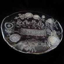 Load image into Gallery viewer, Vintage mid-century folk art style Dalom textured clear pressed glass platter with folded handles featuring a charming gathering of seated figures at a table surrounded by whimsical flowers. Designed by world class glass artisan Goran Warff 1933-2022 for Kosta Boda, Sweden, circa 1970s. A great conversation piece and a spectacular serving tray. One could use this as a centrepiece with pillar candles...the possibilities are endless. Excellent condition, free from chips. Measures 14 inches in diameter
