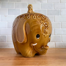 Load image into Gallery viewer, vintage cookie jar of figural elephant features a turbin wearing gentleman sitting on a pillow riding on top which forms the lid&#39;s finial. adorable and the expression on the rider&#39;s face is sassy! The elephant is beautifully decorated in an East Indian motif. Crafted by Noritake, Japan for Giftcraft export. In outstanding condition, free from chips/cracks/wear. We believe this is new old stock. Original sticker present and the bottom has the stamped maker&#39;s mark. Measures 7 1/2 x 5 1/2 x 9 3/4 inches
