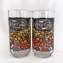 Load image into Gallery viewer, Vintage retro Coca-Cola promotional glass featuring a colourful flower power graphic illustration in an ombre of red, orange and yellow outlined in black. The word &quot;Enjoy&quot; sits above the distinctive Coke logo in a oval medallion reminiscent of a stained glass window. Makers mark is impressed on the bottom, however, we&#39;re unable to assign it to a specific maker.   In excellent, like new condition, free from chips.
