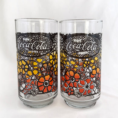 Vintage retro Coca-Cola promotional glass featuring a colourful flower power graphic illustration in an ombre of red, orange and yellow outlined in black. The word 