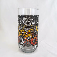 Load image into Gallery viewer, Vintage retro Coca-Cola promotional glass featuring a colourful flower power graphic illustration in an ombre of red, orange and yellow outlined in black. The word &quot;Enjoy&quot; sits above the distinctive Coke logo in a oval medallion reminiscent of a stained glass window. Makers mark is impressed on the bottom, however, we&#39;re unable to assign it to a specific maker.   In excellent, like new condition, free from chips.
