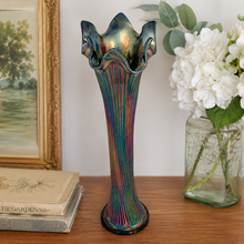 Load image into Gallery viewer, Fenton Fine Rib cobalt blue carnival glass swung vase, full front view showing iridescent purple, teal, and copper lustre on vertical ribbing, with ruffled multi-point rim, circa 1909–1928. Styled on a wood desk with a painting, books and flowers

