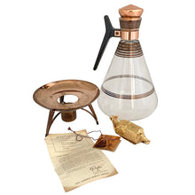 Load image into Gallery viewer, Vintage MCM glass coffee carafe features copper stripes, a black atomic-age bakelite handle, copper cork stopper and metal beauty bowl warmer stand. Crafted by Inland Glass, USA, 1950s. A fabulous mid-century serving piece for yourself or to give as a gift!

In excellent condition. New in box with tags, instructions and 2 candles.

Measures 6 x 9 1/2 inches, spout 2 1/8 inches
