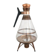Load image into Gallery viewer, Vintage MCM glass coffee carafe features copper stripes, a black atomic-age bakelite handle, copper cork stopper and metal beauty bowl warmer stand. Crafted by Inland Glass, USA, 1950s. A fabulous mid-century serving piece for yourself or to give as a gift!

In excellent condition. New in box with tags, instructions and 2 candles.

Measures 6 x 9 1/2 inches, spout 2 1/8 inches
