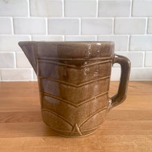 Load image into Gallery viewer, Vintage glossy light brown stoneware pitcher with stacked chevron detail. Crafted by Monmouth Western Stoneware, USA, 1920s. Add this utilitarian piece to your farmhouse decor or art pottery collection!

In excellent condition, no chips/cracks/repairs, age-related crazing. Unmarked.

Measures 4 1/2 x 5 inches
