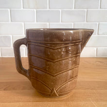 Load image into Gallery viewer, Vintage glossy light brown stoneware pitcher with stacked chevron detail. Crafted by Monmouth Western Stoneware, USA, 1920s. Add this utilitarian piece to your farmhouse decor or art pottery collection!

In excellent condition, no chips/cracks/repairs, age-related crazing. Unmarked.

Measures 4 1/2 x 5 inches
