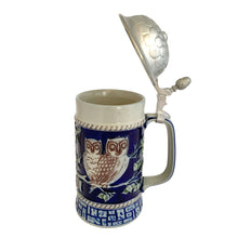 Load image into Gallery viewer, Side of the full stein with pewter lid open, cobalt blue body, two owls on branches relief, rope border, and geometric base band
