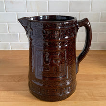 Load image into Gallery viewer, Antique brown glazed stoneware tankard or pitcher, decorated with good luck swastikas. In Native American cultures, the swastika, or Whirling Log as it&#39;s known in Navajo, was a symbol of good fortune, the vehicle of the Culture Hero, or the four winds. This design pre-dates the Nazi era. Crafted by McCoy Pottery, 1920s.

In as found vintage condition, no chips/cracks/repairs. The interior has glaze loss on the bottom and hard water marks.

Measures 7 3/4 x 5 3/4 x 8 1/4 inches (incl. spout/handle)
