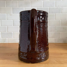Load image into Gallery viewer, Antique brown glazed stoneware tankard or pitcher, decorated with good luck swastikas. In Native American cultures, the swastika, or Whirling Log as it&#39;s known in Navajo, was a symbol of good fortune, the vehicle of the Culture Hero, or the four winds. This design pre-dates the Nazi era. Crafted by McCoy Pottery, 1920s.

In as found vintage condition, no chips/cracks/repairs. The interior has glaze loss on the bottom and hard water marks.

Measures 7 3/4 x 5 3/4 x 8 1/4 inches (incl. spout/handle)

