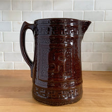 Load image into Gallery viewer, Antique brown glazed stoneware tankard or pitcher, decorated with good luck swastikas. In Native American cultures, the swastika, or Whirling Log as it&#39;s known in Navajo, was a symbol of good fortune, the vehicle of the Culture Hero, or the four winds. This design pre-dates the Nazi era. Crafted by McCoy Pottery, 1920s.

In as found vintage condition, no chips/cracks/repairs. The interior has glaze loss on the bottom and hard water marks.

Measures 7 3/4 x 5 3/4 x 8 1/4 inches (incl. spout/handle)
