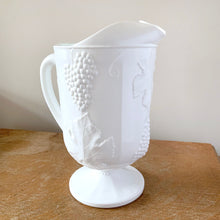 Load image into Gallery viewer, The words &quot;stunning&quot; and &quot;elegant&quot; embody this incredible milk glass pitcher in the &quot;Harvest&quot; pattern of grapes and vines. This is the largest version in this series holding 72oz. Made by Colony (Indiana) Glass Co. Circa 1966. This pitcher would look amazing on any tablescape or use it for a beautiful floral bouquet.  In excellent condition, no chips or cracks.  Measures 6 x 10 3/8 inches
