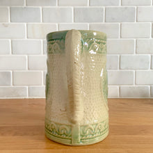 Load image into Gallery viewer, Antique grazing cows salt glazed yellow ware ceramic pitcher with decorative green medallion, rim and base. Crafted by Hull Pottery, USA, 1920s. This utilitarian piece nicely complement any farmhouse or cottage kitchen!

In as found vintage condition, no chips/repairs, hairline crack near the spout (see photos), age-related wear to the exterior. Unmarked.

Measures 6 1/2 x 6 1/2 inches (incl. handle)

Capacity approximately 32 ounces
