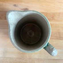 Load image into Gallery viewer, Antique grazing cows salt glazed yellow ware ceramic pitcher with decorative green medallion, rim and base. Crafted by Hull Pottery, USA, 1920s. This utilitarian piece nicely complement any farmhouse or cottage kitchen!

In as found vintage condition, no chips/repairs, hairline crack near the spout (see photos), age-related wear to the exterior. Unmarked.

Measures 6 1/2 x 6 1/2 inches (incl. handle)

Capacity approximately 32 ounces
