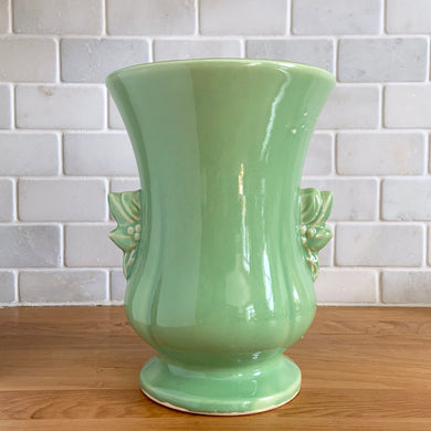 Beautiful vintage Art Deco pale green handled trumpet vase #282 features berry and leaf handles. Crafted by McCoy Pottery, 1946. This vase is must for any art pottery collector. A lovely way to enhance your home's decor or to give as a gift!

In great vintage condition, chip to underside of foot, no cracks/repairs. Typical manufacturer's glaze pops/defects. Maker's mark on the bottom.

Measures 6 x 8 1/8 inches (incl. handle/spout)